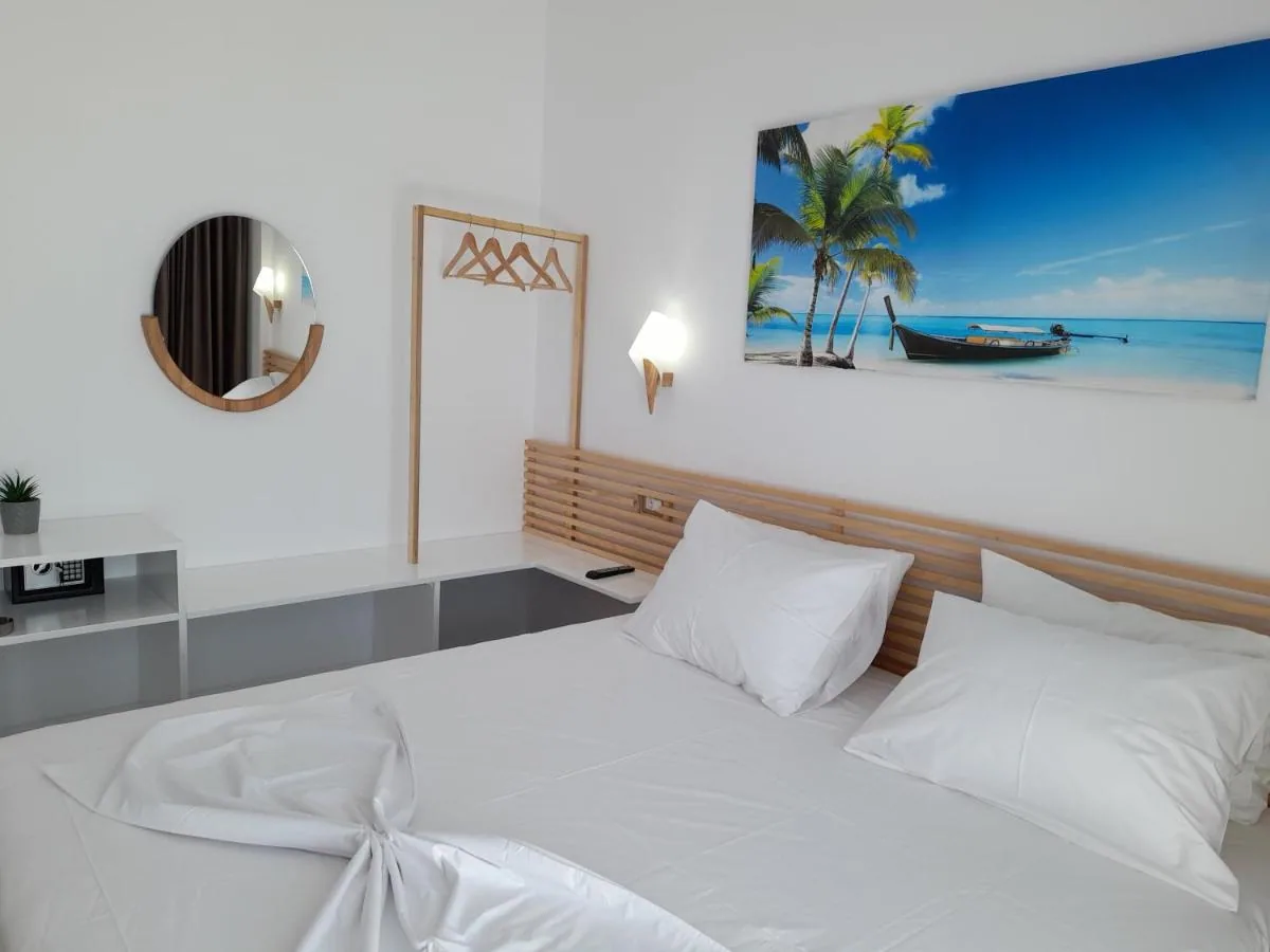 A white double room with a slatted light-oak headboard, a round timber-framed mirror and a wall-mounted canvas print.