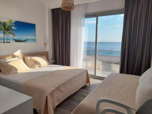 A sea-view room with a double bed and a second bed, its balcony door opening onto Livadhi Beach and the Ionian beyond.