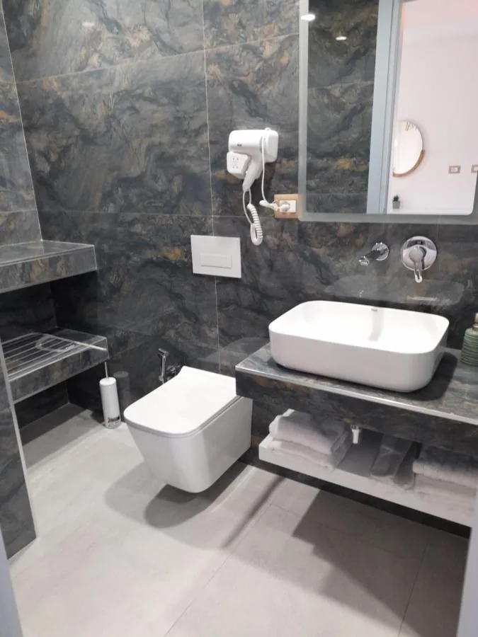 The same stone behind a white basin set on the stone shelf and a wall-hung WC, towels folded beneath.