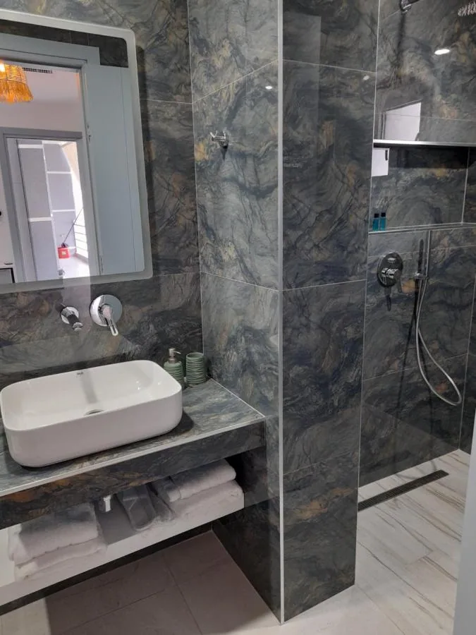 A bathroom lined wall to ceiling in veined blue-grey stone, with a walk-in shower and a white vessel basin.