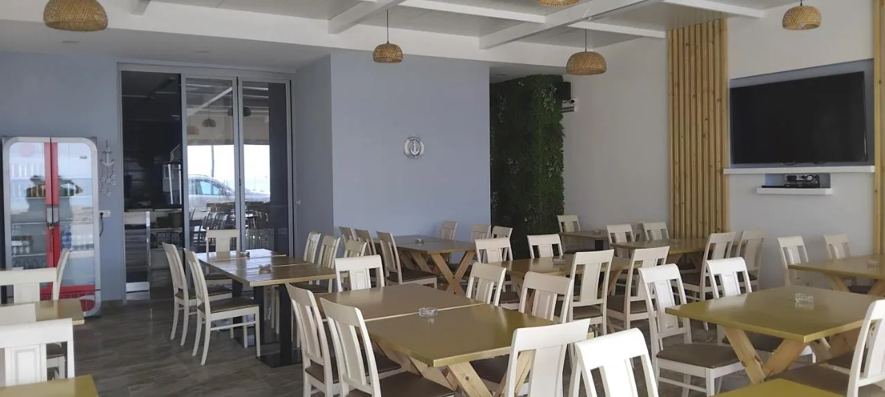 The dining room at Anxhelos: slate-blue walls, white beamed ceiling, rattan pendant lamps and timber tables with white chairs.