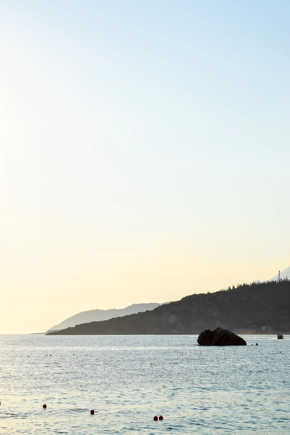 The rock standing offshore at Livadhi, with the cypress-topped ridge running out to the point.