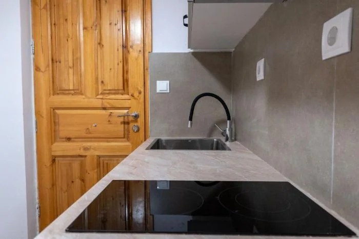 An L-shaped kitchen counter with a sink, a black ceramic hob and a pine door beside it