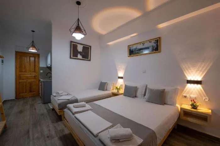 A single bed and a double bed side by side under wall uplights, a framed picture above each and a wooden floor