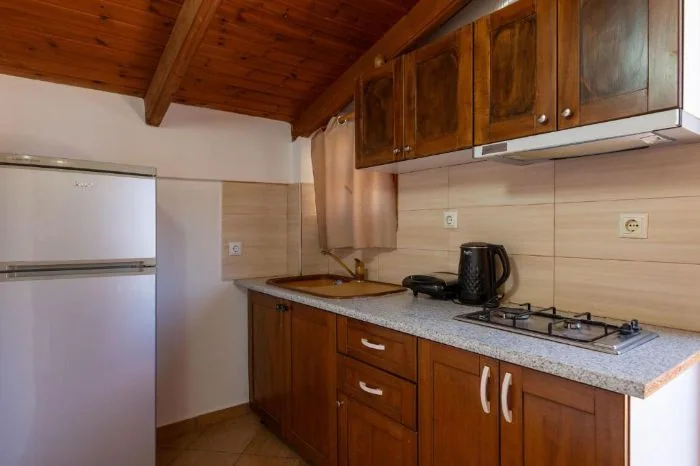 A kitchen with dark timber units, a four-burner gas hob and a tall fridge-freezer under the boarded roof