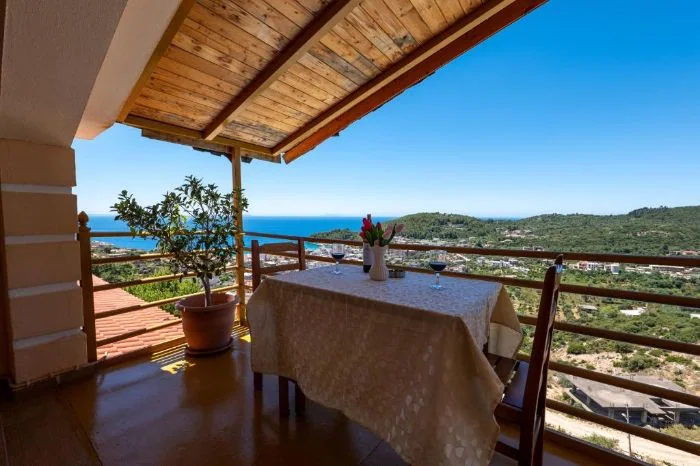 A table laid on the penthouse terrace under the boarded eaves, the bay and the wooded headland beyond the rail