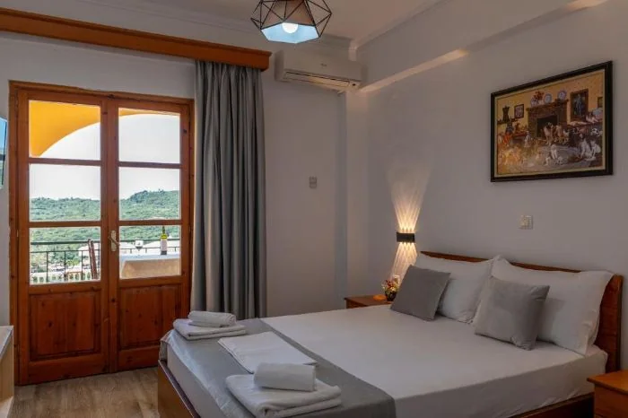 A double bed beside a pair of glazed timber balcony doors, green hillside through the glass