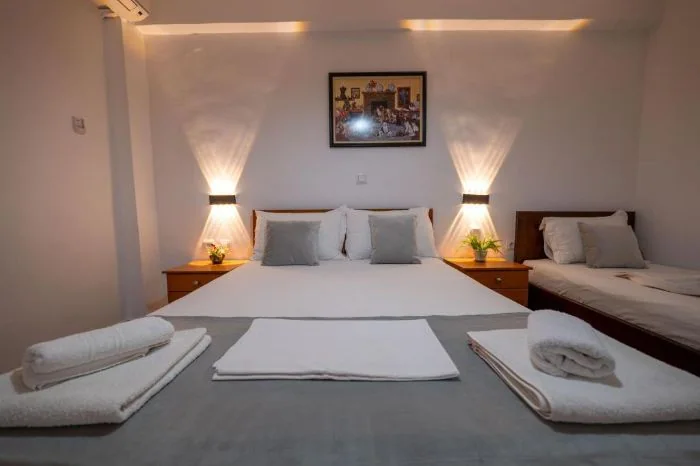 A double bed and a single bed with white linen, uplighting on the wall and a framed picture above the double