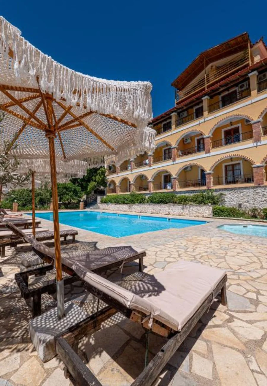 A fringed parasol and two loungers on the flagstone deck with the yellow arcade rising behind them