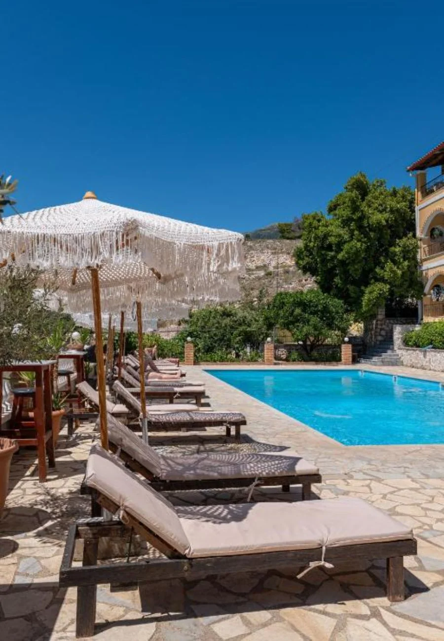 A row of loungers along the pool under an open fringed parasol, the hillside beyond