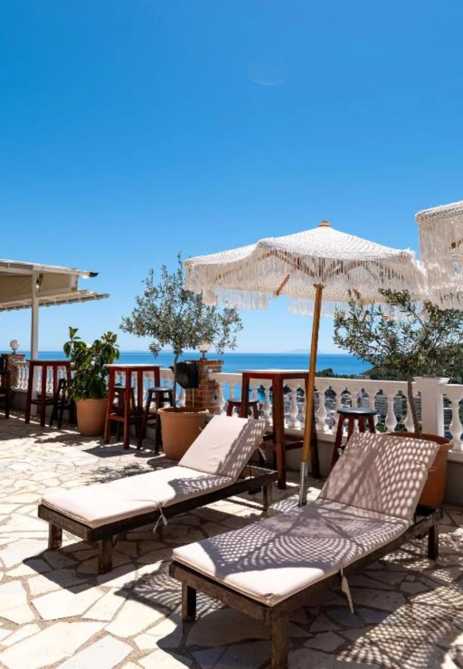 Two loungers and an open parasol on the upper terrace with an olive tree and the sea on the horizon