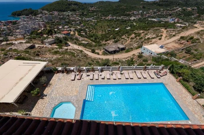 Looking down from the hotel roof over the pool deck and its row of loungers to Himarë town, the bay and the headland beyond