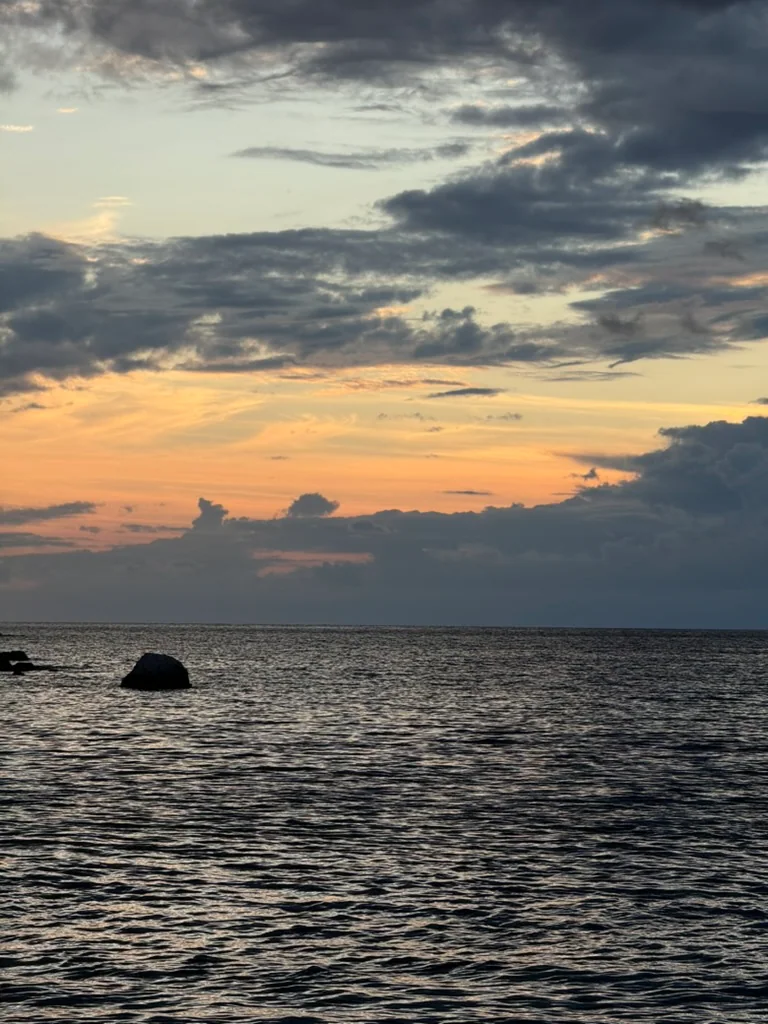 Dusk over the Ionian off Himarë, an amber band under indigo cloud and a rock standing out of dark water