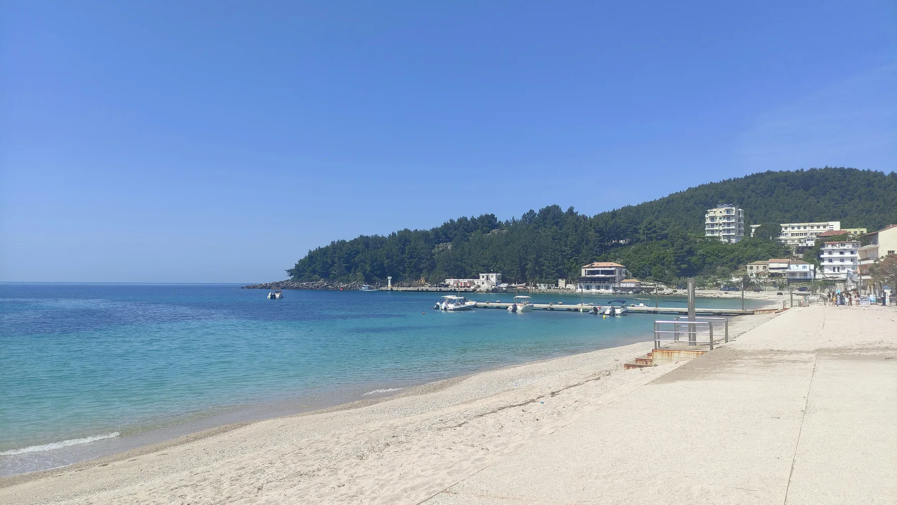 The shore at Himarë with the jetty and moored boats, the wooded headland behind and the town climbing the hill