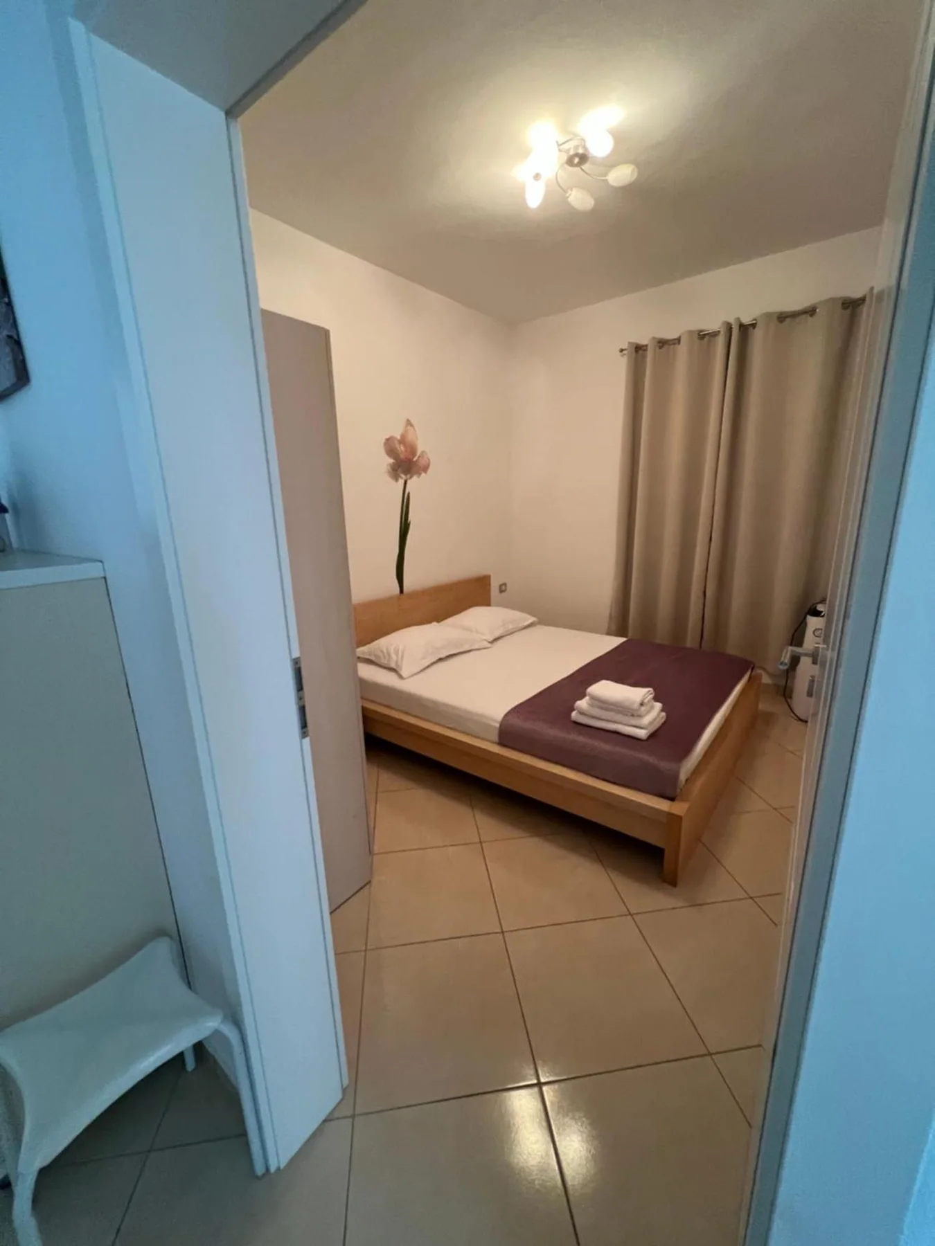 The bedroom seen from the hall through an open door, with the bed made up and a curtained window beyond
