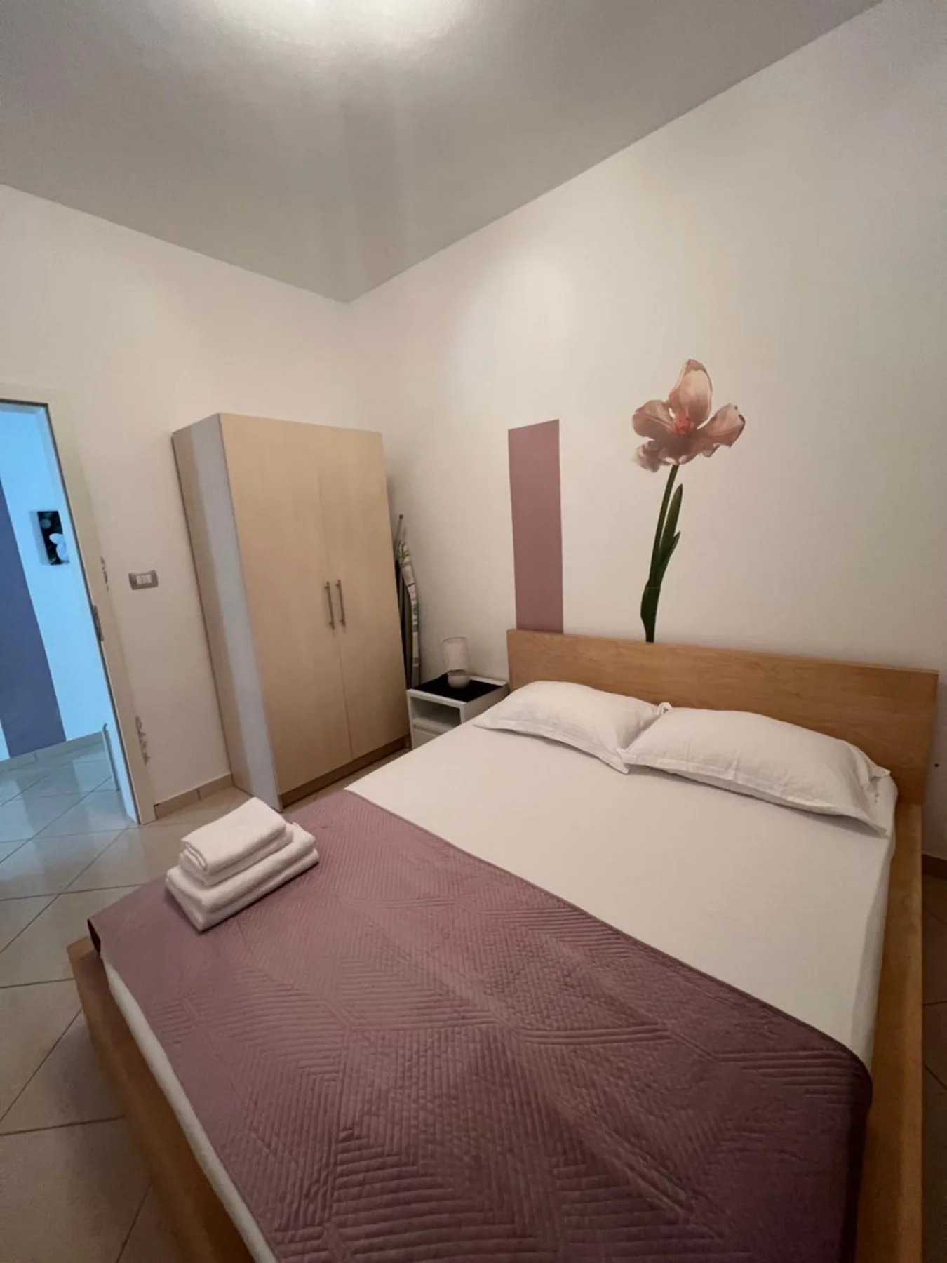 The bedroom with a wooden-framed queen bed, folded towels on the cover, a tall wardrobe and an iris on the wall