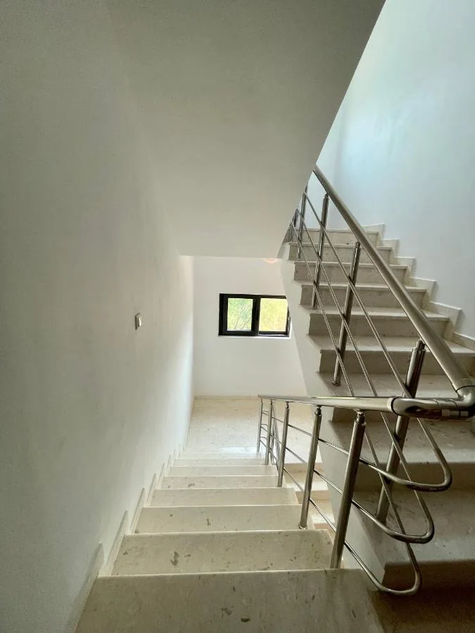 A pale travertine staircase with a stainless steel balustrade turning at a landing, lit by a small window on the half-landing wall