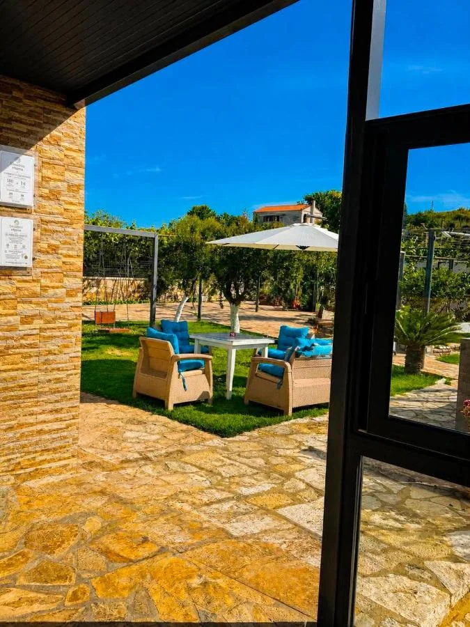 Two wicker armchairs and a wicker sofa with blue cushions around a white table on the grass, a parasol standing open on the paving behind them, beside a flagged stone terrace