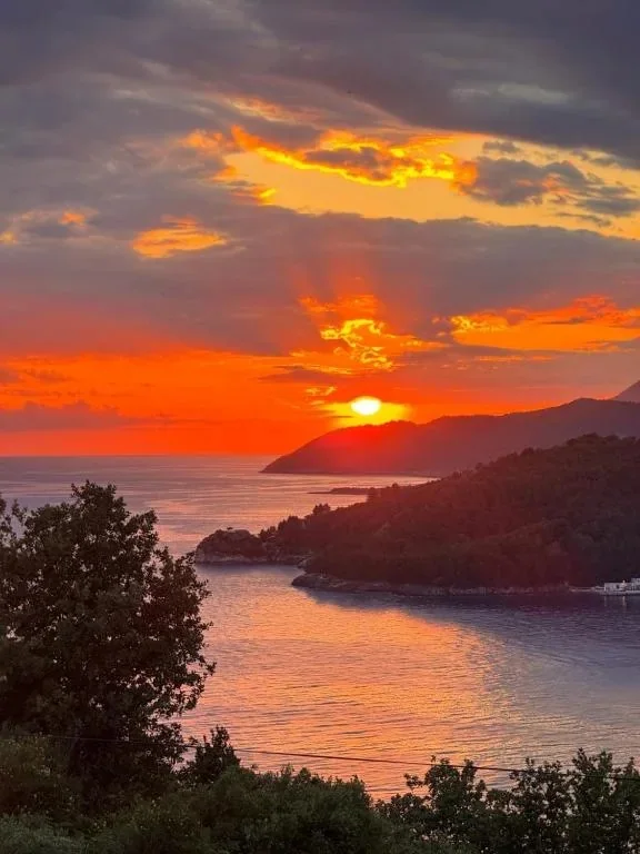 The sun dropping behind the wooded headland across the bay, the sky burnt orange and the water below it still