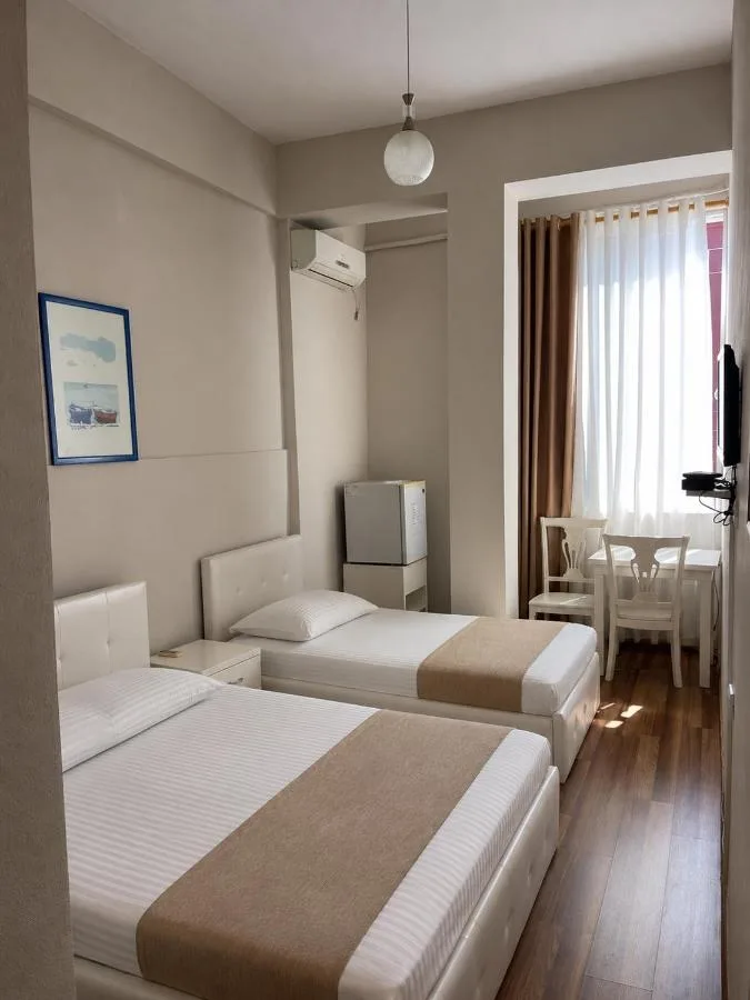 Two single beds with upholstered headboards, a framed print, wardrobe recess, fridge and a desk by the curtained window.