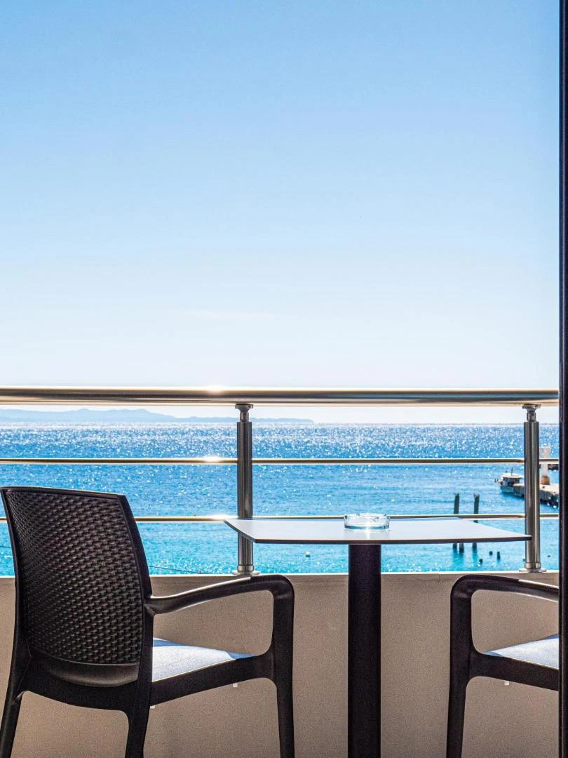 A table and two chairs on a balcony at Endless Blue Himara, looking over the open Ionian to the far shore on the horizon