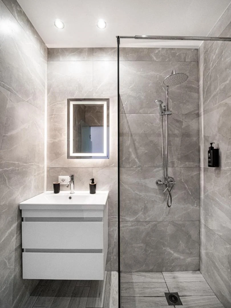 A tiled bathroom with a walk-in rain shower, a backlit mirror and a wall-hung basin unit
