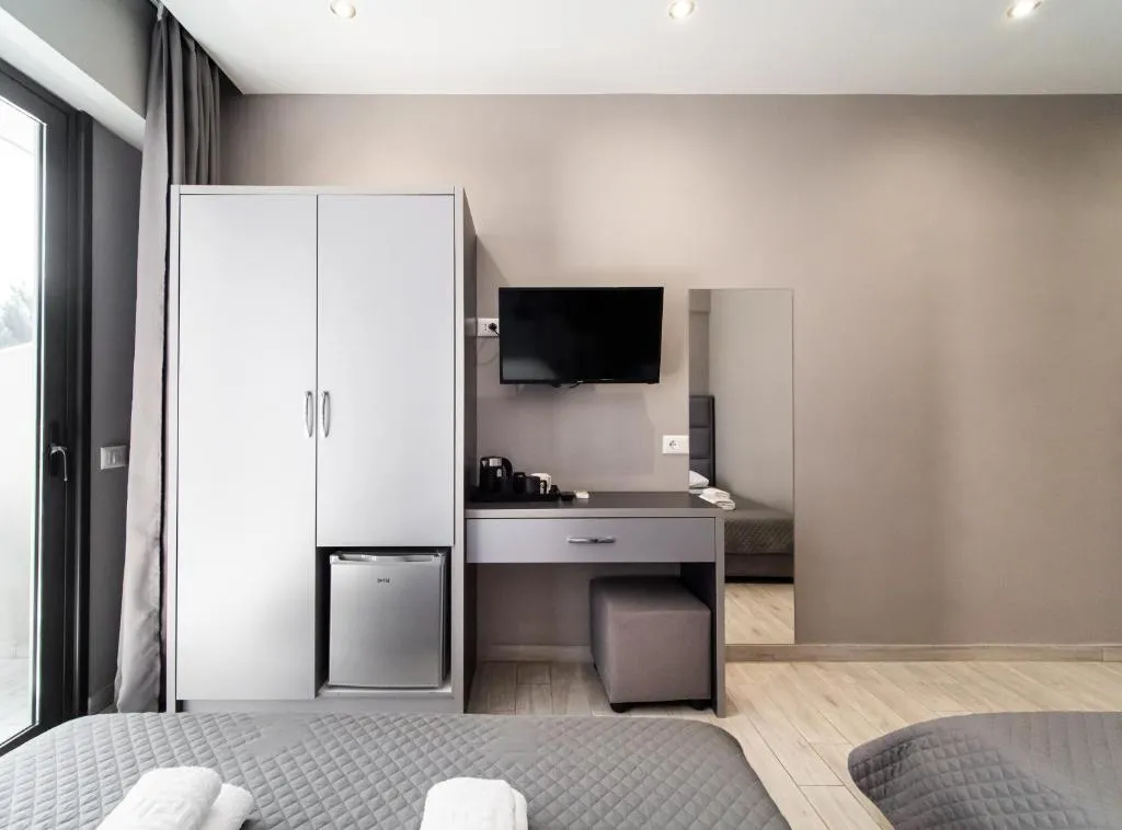 A guest room wardrobe with a refrigerator in a recess in its base, a desk with a kettle and cups, and a wall-mounted television