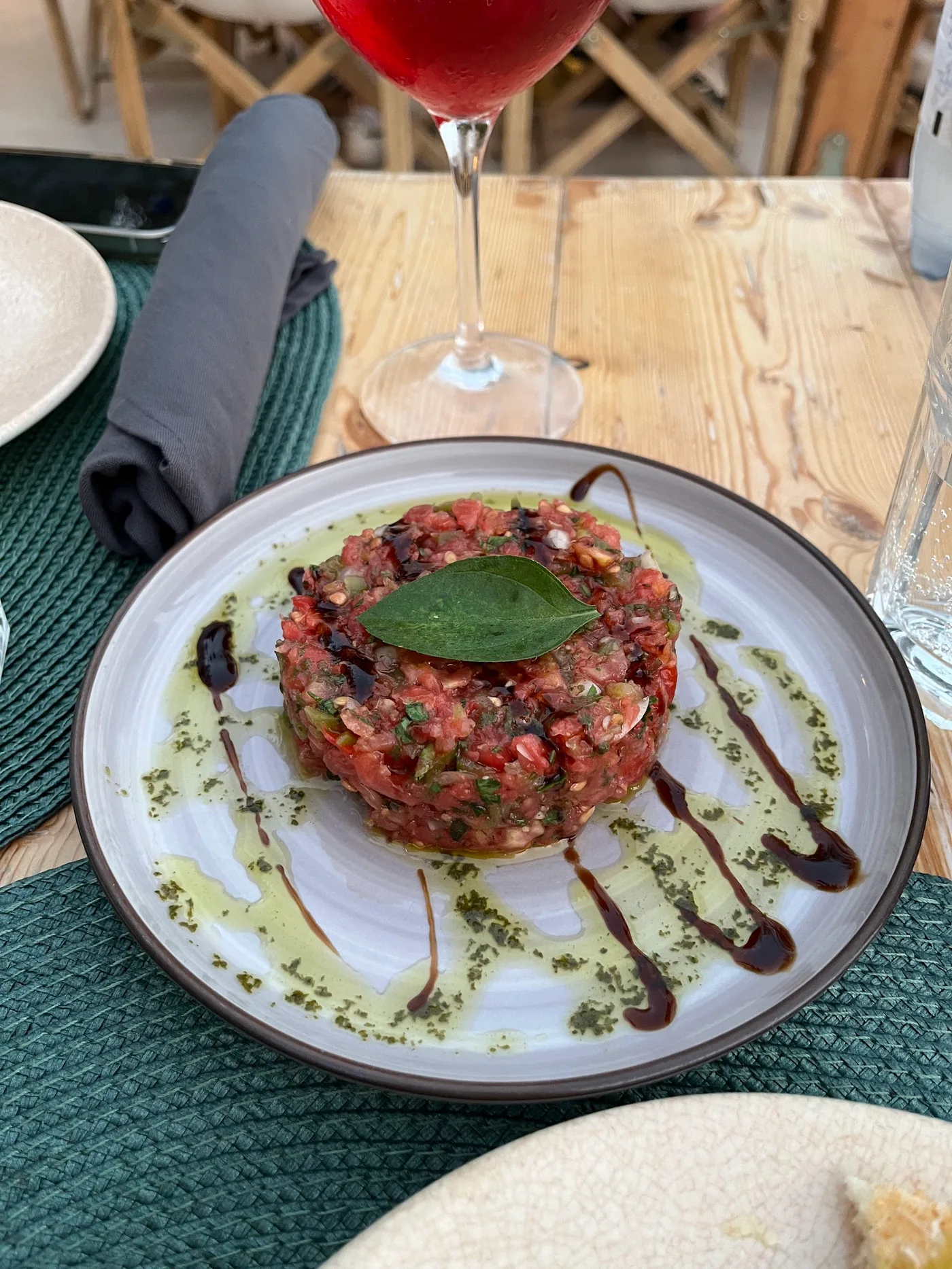 Tomato tartare under a single basil leaf, ringed with green herb oil and balsamic, at Fig & Olive, Himarë