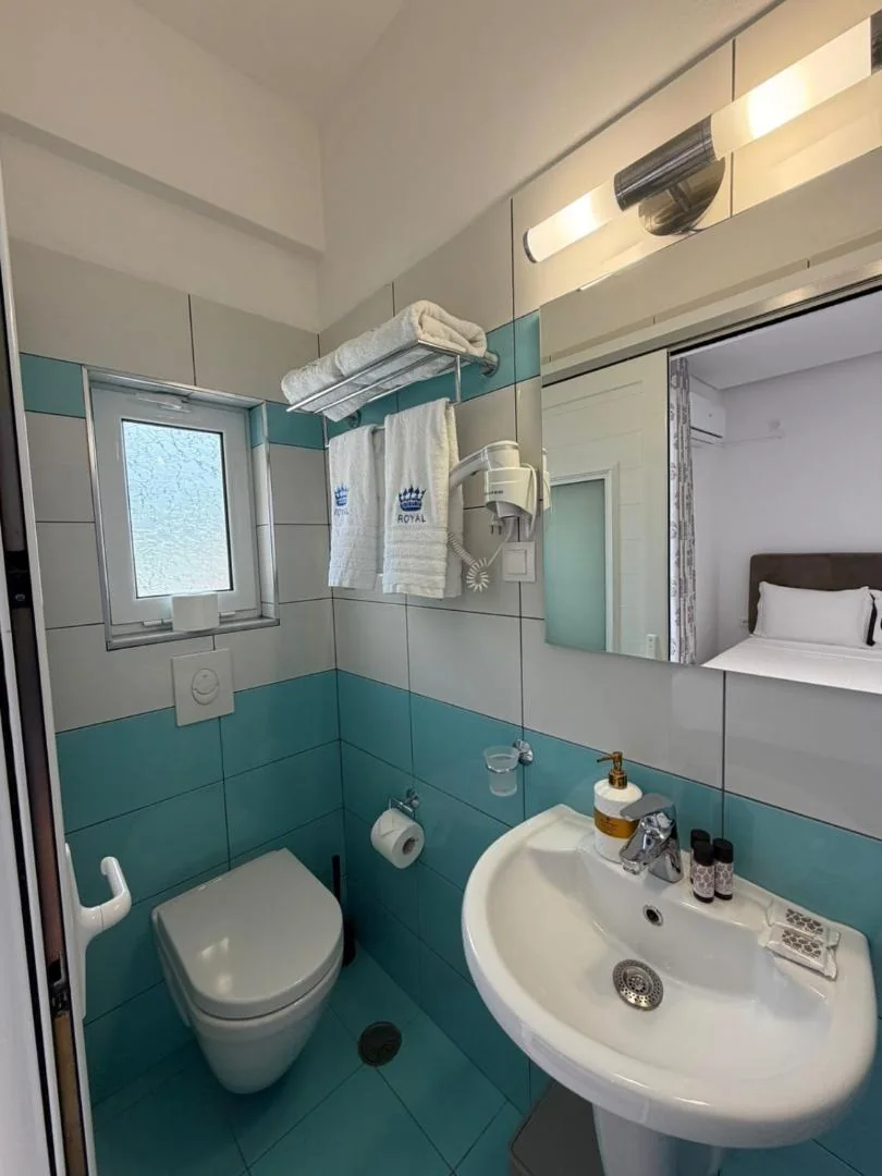 A bathroom tiled in turquoise below and white above, a crown and the word ROYAL embroidered on the hanging towels