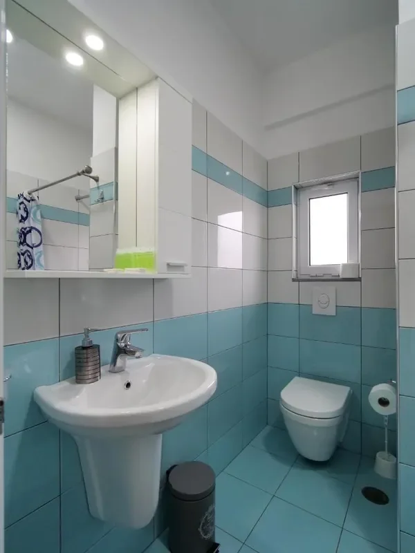 A second turquoise-tiled bathroom with a mirrored cabinet over the basin and a window on the far wall