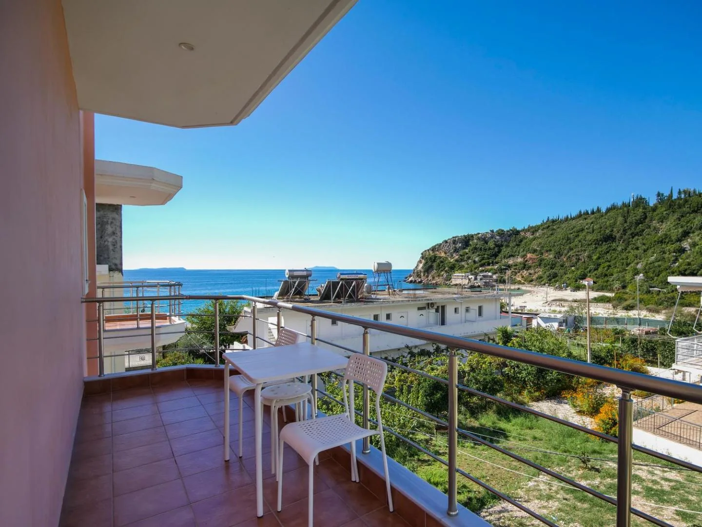 The view from a hotel balcony over low roofs to the bay, a wooded headland to the right and Livadhi Beach beyond