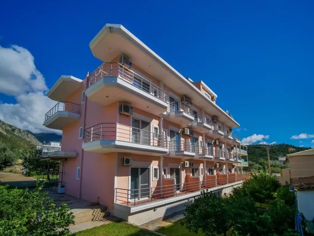 The three-storey rendered facade of Himara Royal Hotel, stacked balconies on every floor, the hillside behind