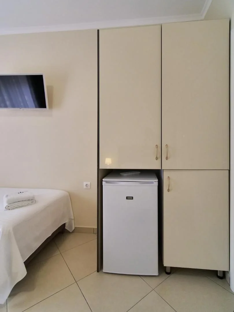 A fitted cabinet with a refrigerator beneath it and a flat-screen television on the wall beside a bed