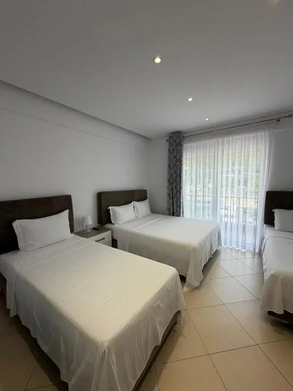 Three beds in a tiled room with a curtained balcony door at the far end