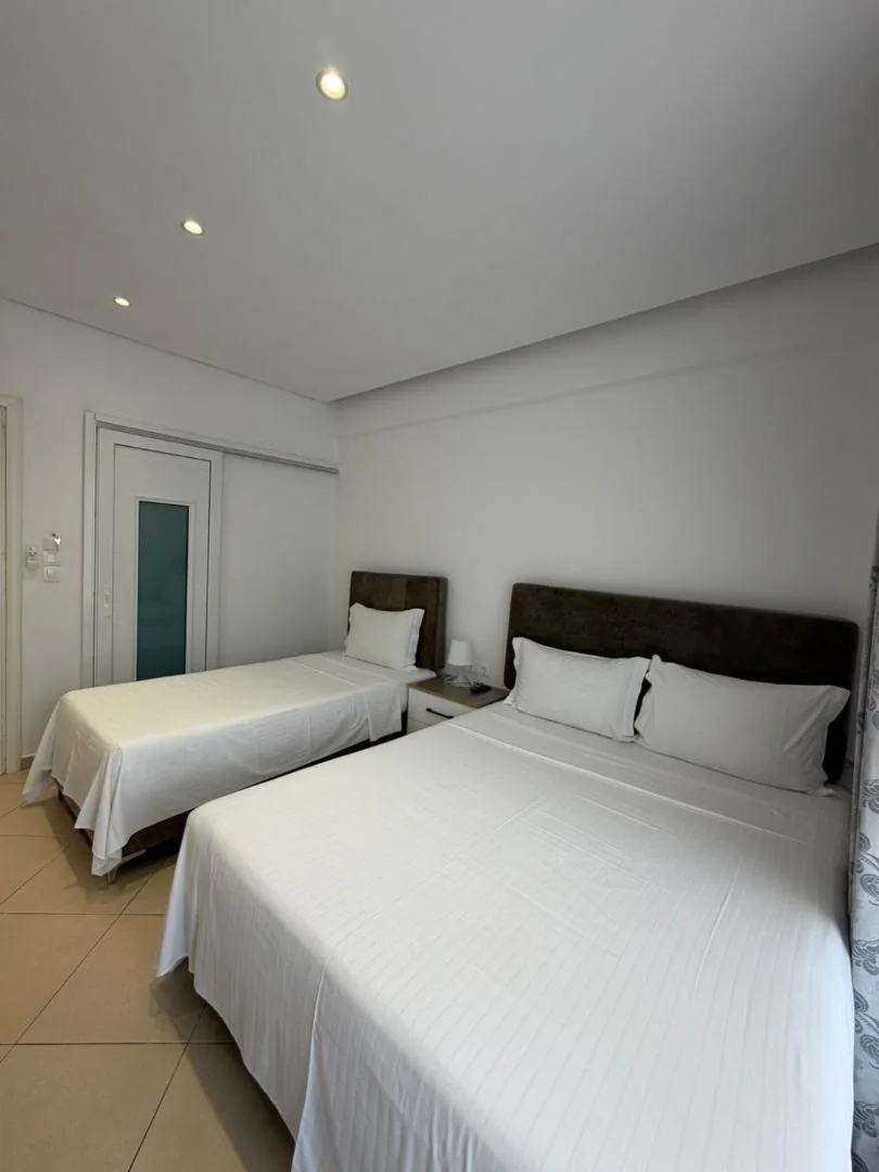 A twin bed and a queen bed with brown upholstered headboards in a white room, an internal sliding door with a frosted pane at the left