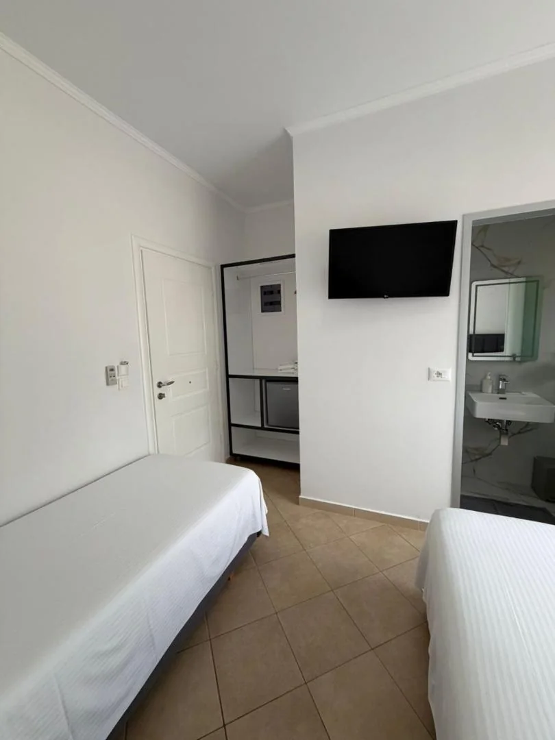 A twin room with a flat-screen television, a refrigerator in a fitted niche and an opening onto a marble-effect bathroom