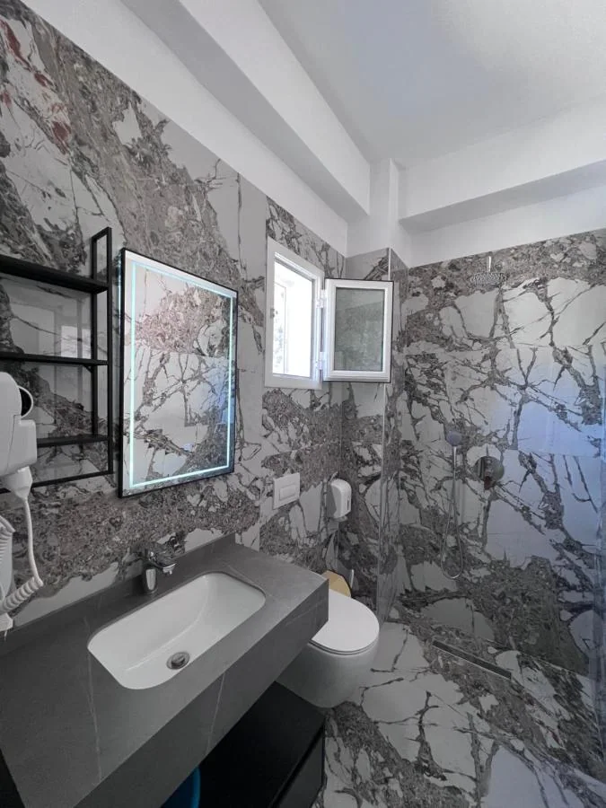 The veined marble bathroom of the Triple Room, with a wall-hung basin and a lit mirror