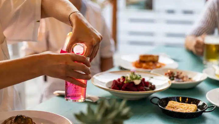 A pink drink being poured from a glass bottle at a laid table of beetroot salad and small plates