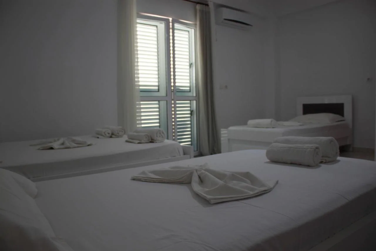 White beds in a white room with pale blue louvred balcony doors and a wall-mounted air-conditioning unit