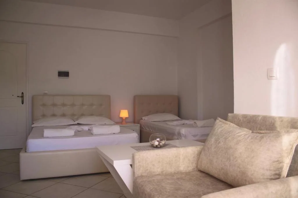A double bed with a buttoned cream headboard, a single bed with a plain padded one, a small lamp between them and a sofa in the foreground