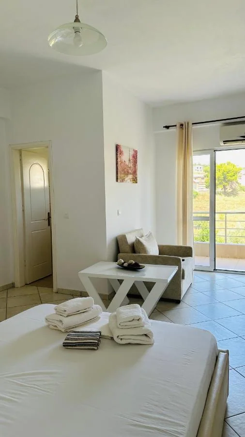 The end of a bed, a sofa and a coffee table beside a sliding balcony door with a green hillside beyond