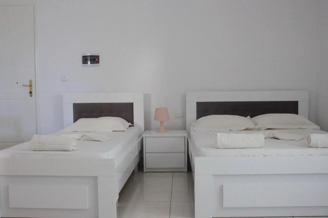 A single bed and a double bed with dark padded headboards and a small pink shaded lamp between them
