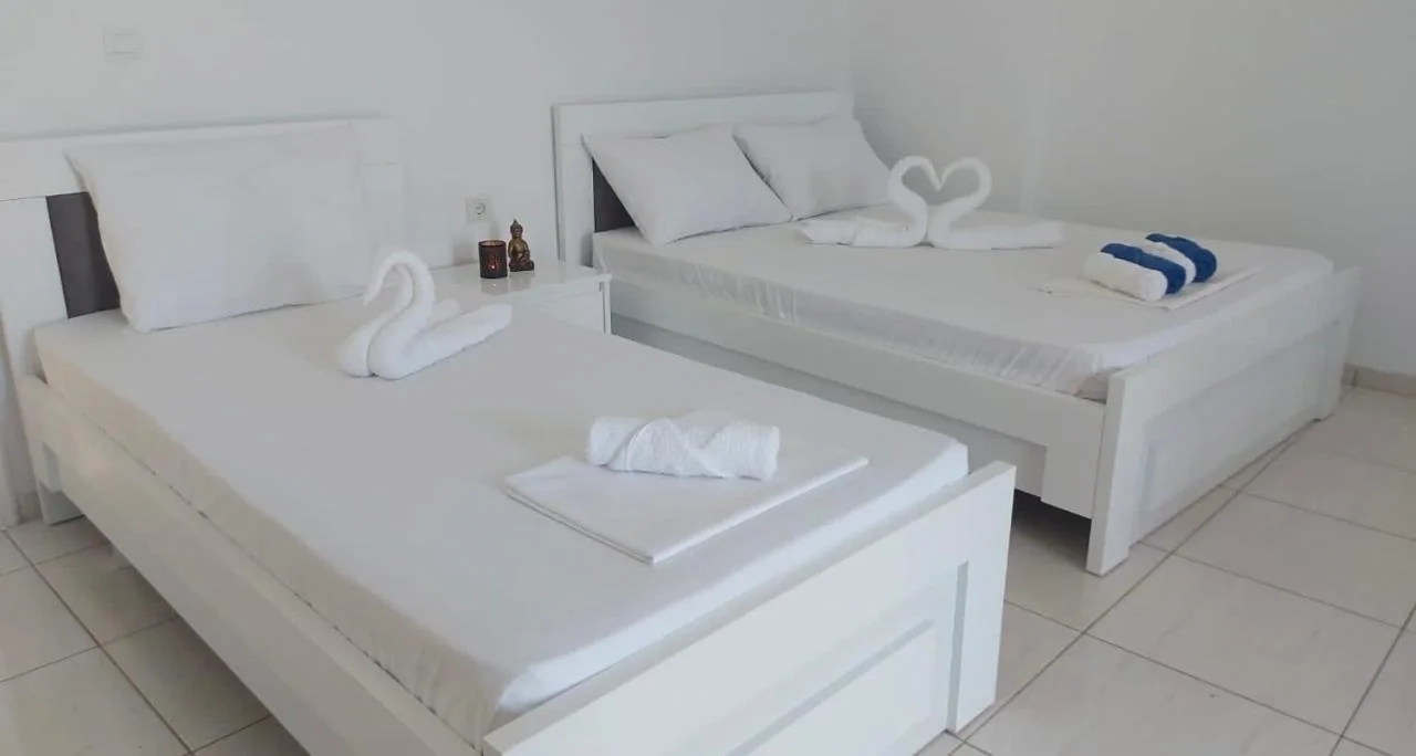 A room with a single bed and a double bed side by side, white bedsteads, white walls and a tiled floor