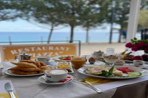A breakfast table laid on the terrace, with the terracotta Piazza board and the beach behind it