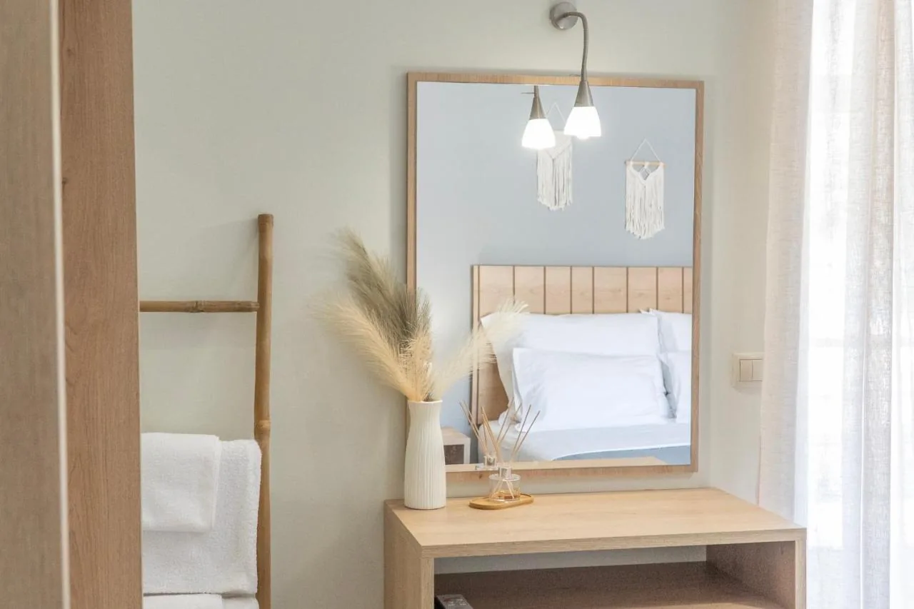 An oak console table with pampas grass in a ribbed vase, below a framed mirror reflecting the bed and two macramé hangings