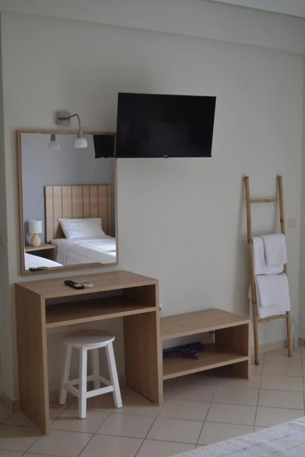 A pale oak desk and stool below a wall-mounted flat-screen television, a mirror reflecting a single bed, and a timber ladder hung with towels