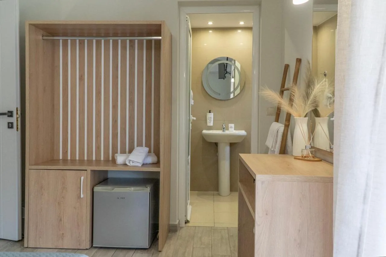 An open oak wardrobe with a fluted back and a small fridge below it, with a tiled bathroom and round mirror through the doorway beyond