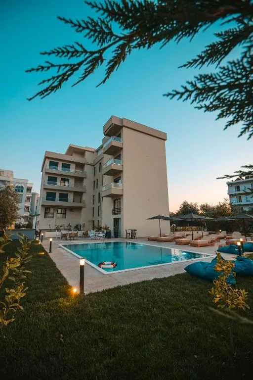 The five-storey hotel block lit at dusk above its pool, seen across the lawn