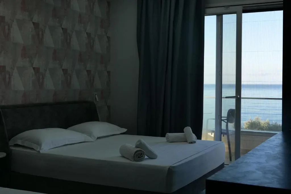 A room with a rose and grey triangle feature wall, a bed and a balcony door filled with open sea