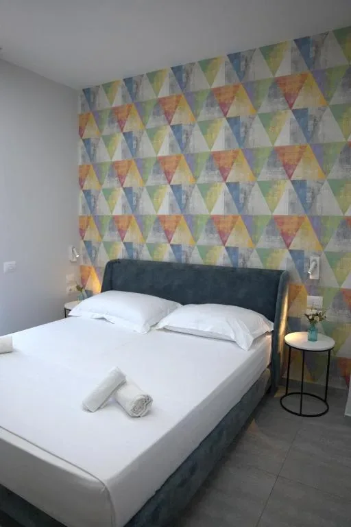 A double bed with a navy velvet headboard against a multicoloured triangle feature wall
